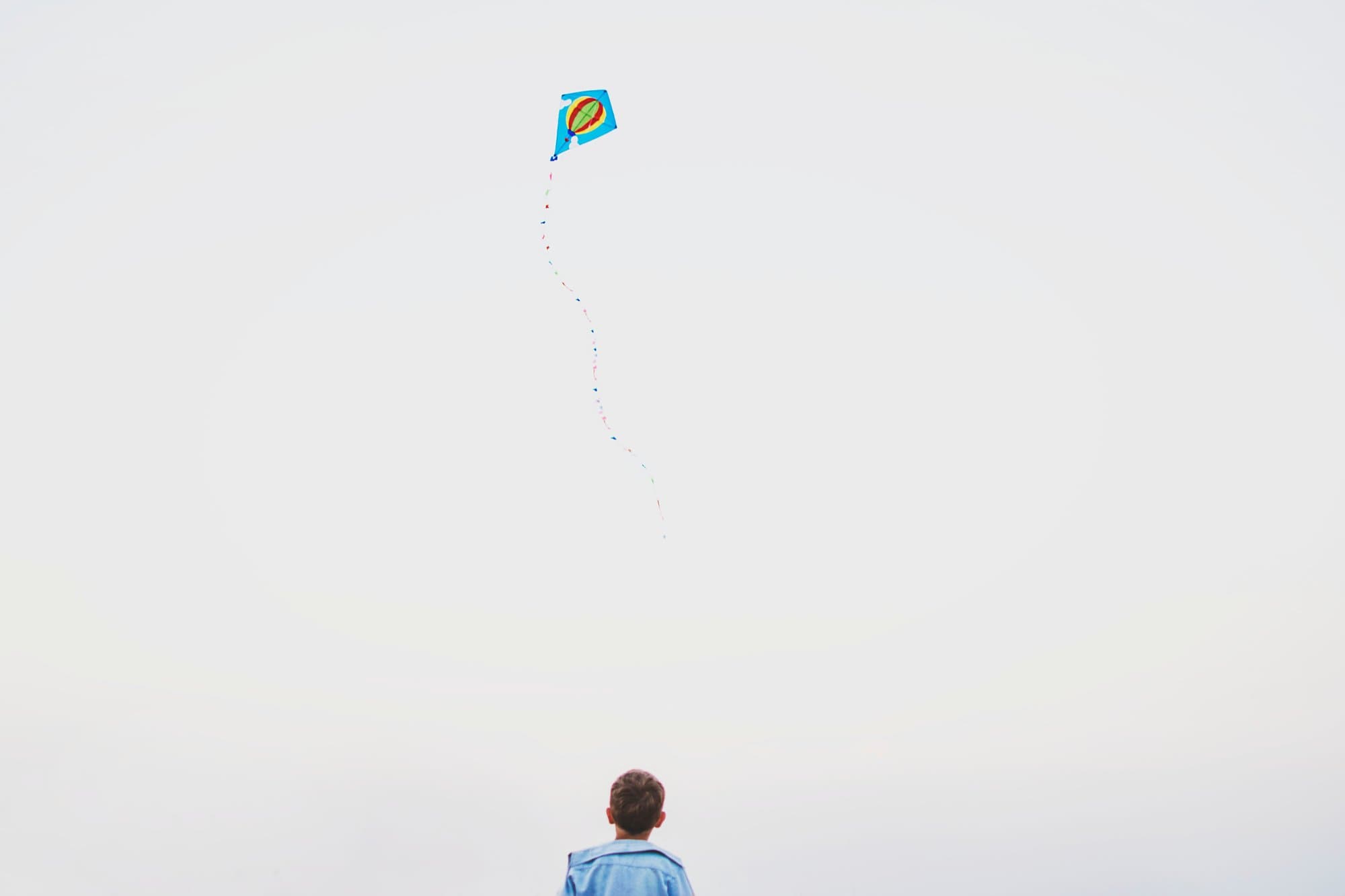 Child flying a kite against a white sky