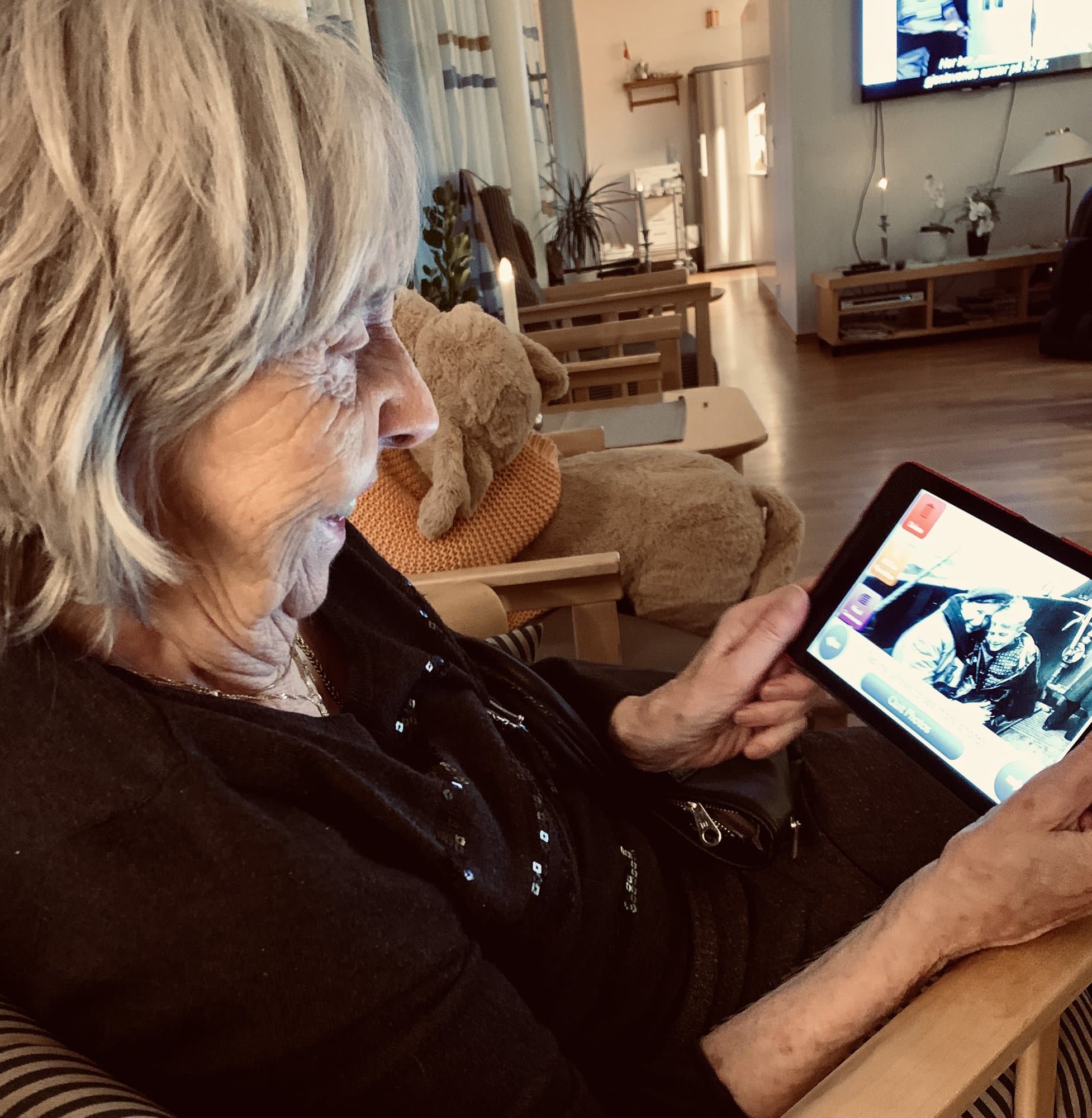 Older woman in her armchair looking at a photo in JodaCare on a tablet